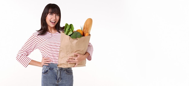 Heureuse femme asiatique tenant un sac en papier plein d'épicerie de légumes frais isolé sur fond blanc de l'espace de copie.