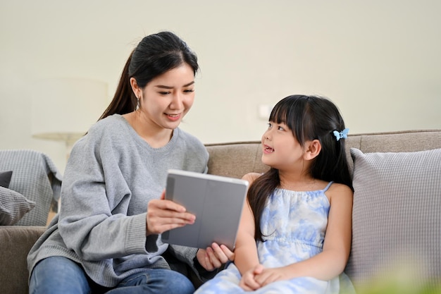 Heureuse femme asiatique utilise une tablette numérique tout en se relaxant dans le salon avec sa sœur