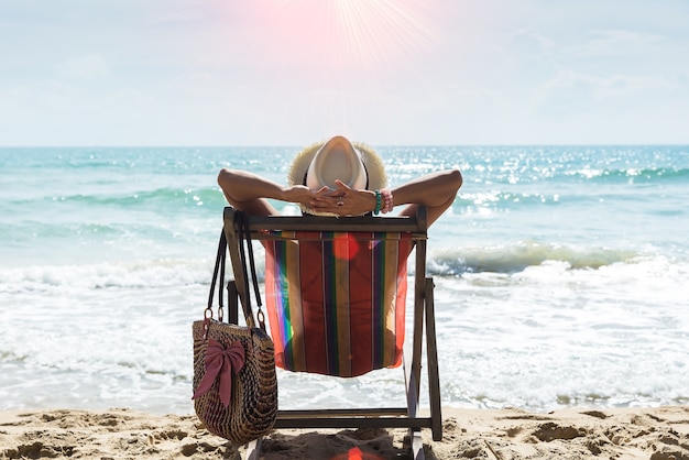 Heureuse femme assise sur une chaise longue à la plage, se détendre sur la plage tropicale. Concept de voyage