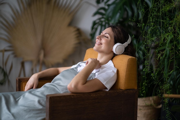 Heureuse femme assise sur le fauteuil dans le jardin de la maison, écoutez la radio en ligne et profitez d'une bonne journée