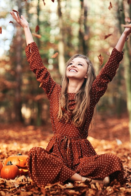 Heureuse femme assise et jetant des feuilles d'automne dans la forêt