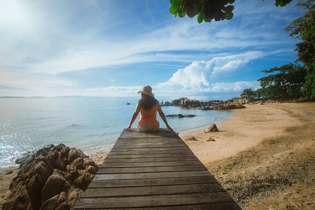 Photo heureuse femme assise sur un pont en bois avec vue sur la mer flou artistique avec bruit