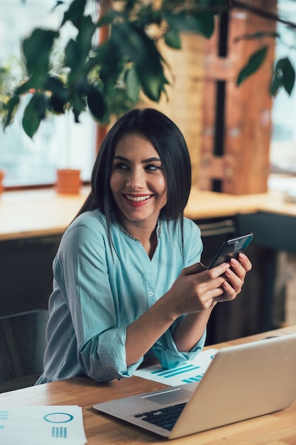 Heureuse femme assise avec un smartphone et faisant demi-tour avec un sourire