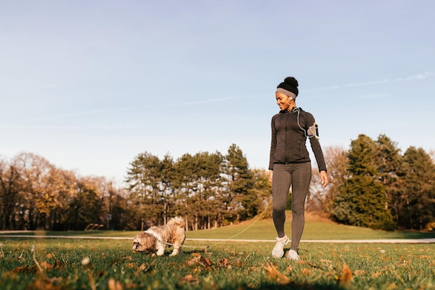 Heureuse femme athlétique afro-américaine appréciant tout en promenant son chien dans la nature