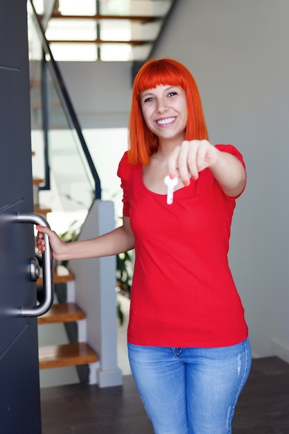 Heureuse femme aux cheveux rouges ouvrant sa maison