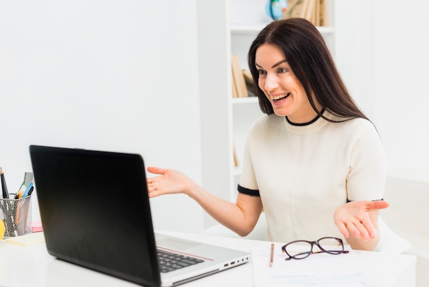 Heureuse femme ayant un appel vidéo à l&#39;aide d&#39;un ordinateur portable au bureau