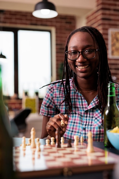 Heureuse femme ayant un pion à la main tout en jouant aux échecs et souriant chaleureusement à la caméra. Joueur de jeux de société à l'air intelligent tenant une pièce d'échiquier pensant au prochain mouvement tout en profitant d'une activité de loisirs.