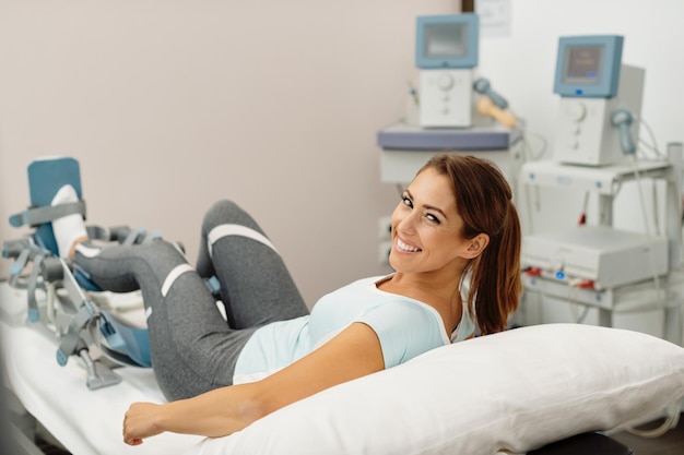 Heureuse femme ayant une thérapie de rééducation des jambes avec un appareil arthromot au spa de santé