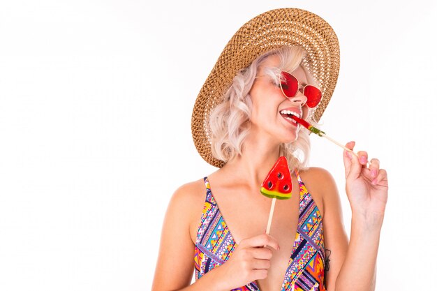 Heureuse femme blonde caucasienne se tient en maillot de bain avec des sucettes de pastèque et des sourires isolés