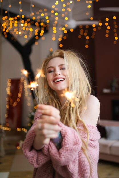 Heureuse femme blonde joyeuse fête le nouvel an par l'arbre de Noël