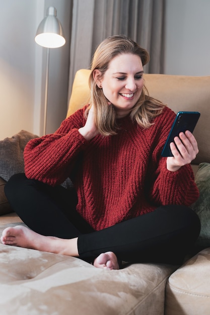 Heureuse femme blonde à la maison à l'aide de smartphone