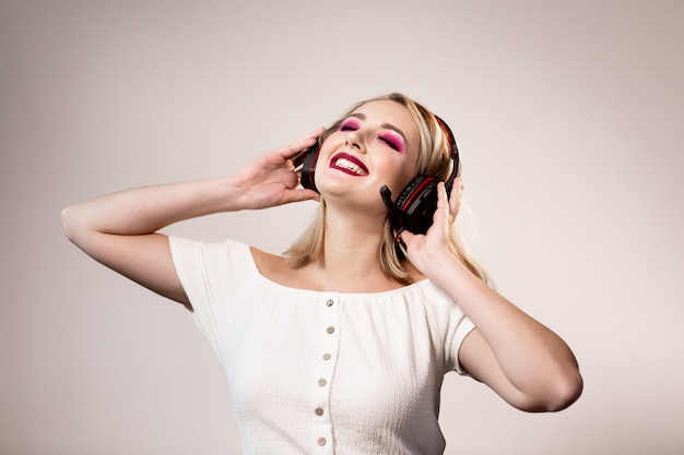 Heureuse femme blonde avec un maquillage lumineux et des écouteurs aime la musique sur un fond simple