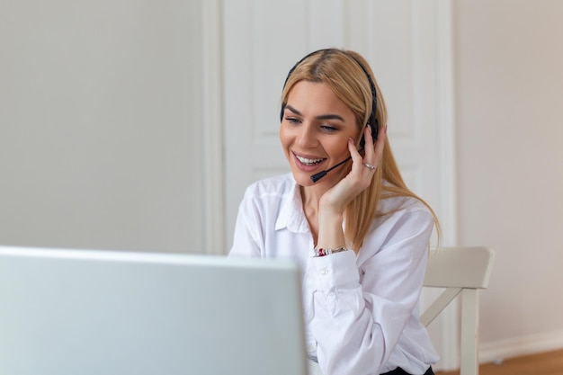 Heureuse femme blonde portant des écouteurs et un microphone regardant la webcam souriant à la caméra en riant lors d'une réunion virtuelle ou d'un appel vidéo Employé travaillant à domicile Vue de l'écran prise de vue en tête