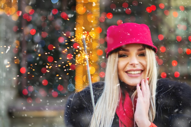 Photo heureuse femme blonde s'amusant avec des lumières étincelantes à la foire de noël. espace pour le texte