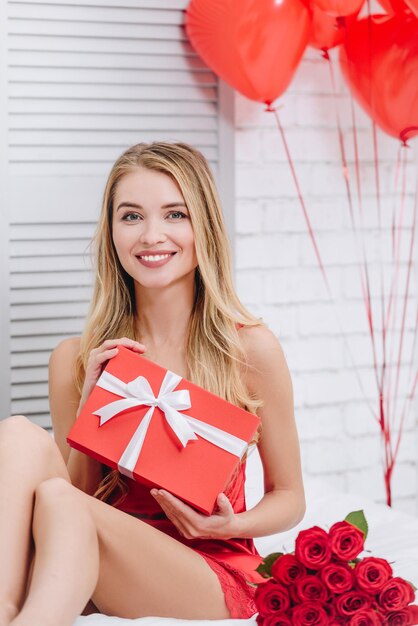 Heureuse femme blonde souriante avec boîte-cadeau en regardant le concept de la saint-valentin de la caméra