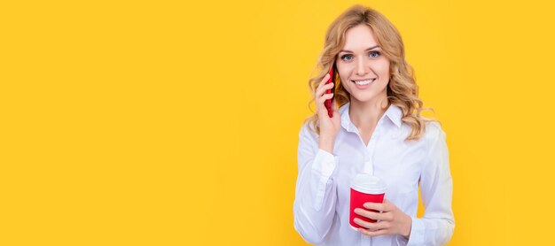 Heureuse femme blonde avec une tasse de café parlant au téléphone sur fond jaune Bannière de portrait de visage isolé de femme avec espace de copie maquette