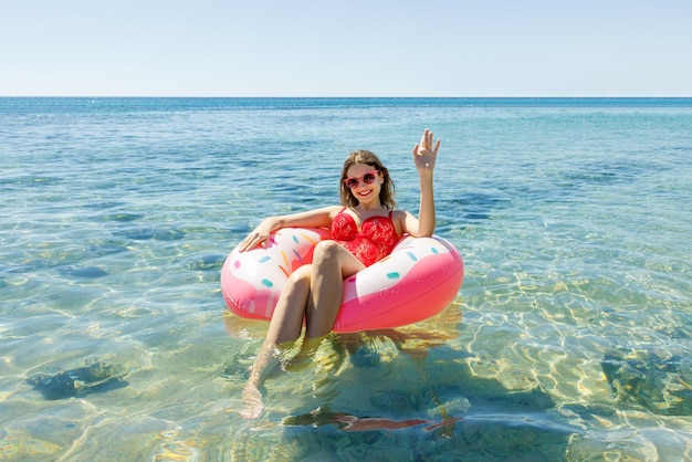 Heureuse femme brune en beignet gonflable rose en journée ensoleillée d'été