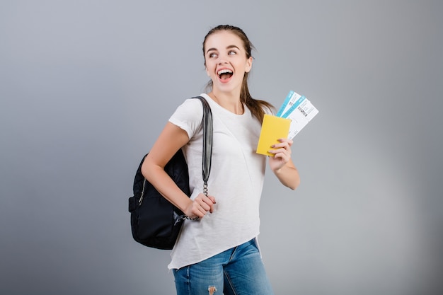 Heureuse femme brune avec des billets d'avion dans le passeport et sac à dos isolé sur gris