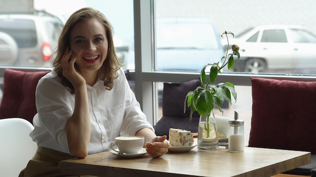 Heureuse femme brune buvant du café et parlant au téléphone portable au café.