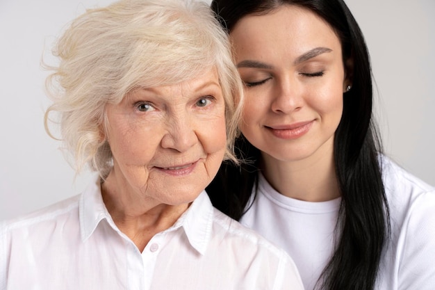 Heureuse femme brune étreignant avec sa belle mère âgée isolée sur fond de mur blanc Concept de relations familiales