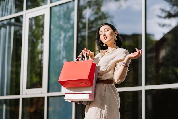 Heureuse femme brune tenant des sacs à provisions à l'extérieur. Shopoholic femme satisfaite des achats