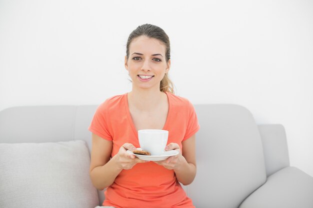 Heureuse femme brune tenant une tasse, souriant à la caméra