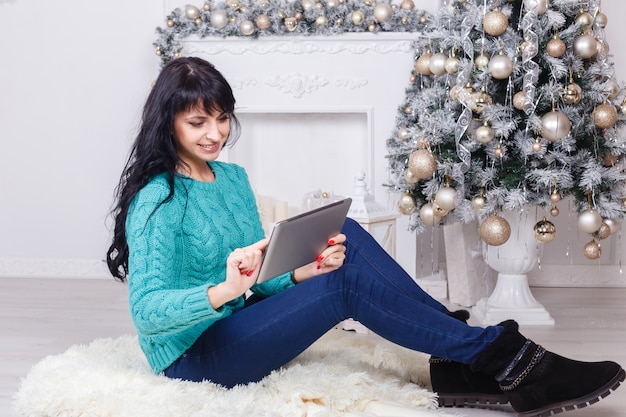 Heureuse femme caucasienne, assis à l'intérieur dans la décoration de Noël à l'aide d'une tablette blanche.