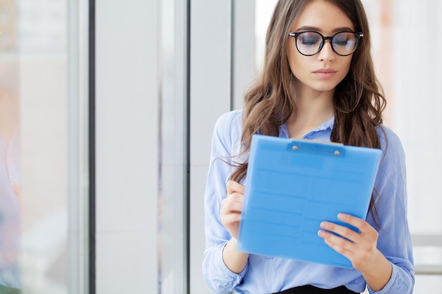 Heureuse femme charmante tenir presse-papiers écrire la liste de plans bonne humeur au bureau