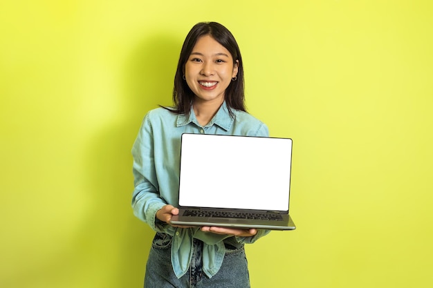 Heureuse femme coréenne montrant un écran vide d'ordinateur portable sur fond jaune