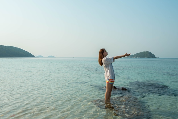 Heureuse femme debout les bras tendus sur la plage en mer