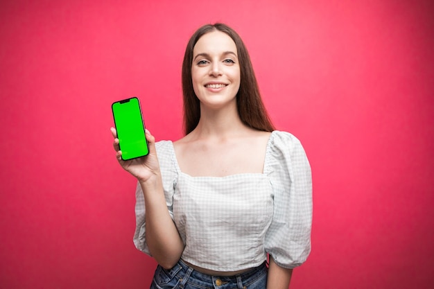 Heureuse femme debout et tenir le smartphone sur fond rose. Écran de téléphone à écran vert