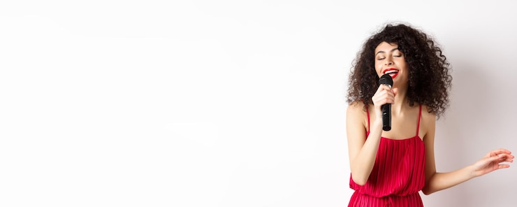 Photo heureuse femme élégante en robe rouge jouant avec microphone chantant karaoké et souriant debout au-dessus