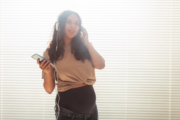 Heureuse femme enceinte aux cheveux bouclés, écouter de la musique dans des écouteurs avec espace de copie.