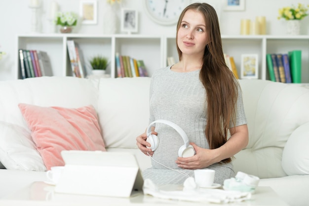 Heureuse femme enceinte avec un casque sur le ventre posant à la maison