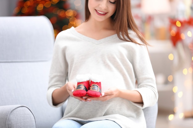 Heureuse femme enceinte avec des chaussons pour bébé à la maison