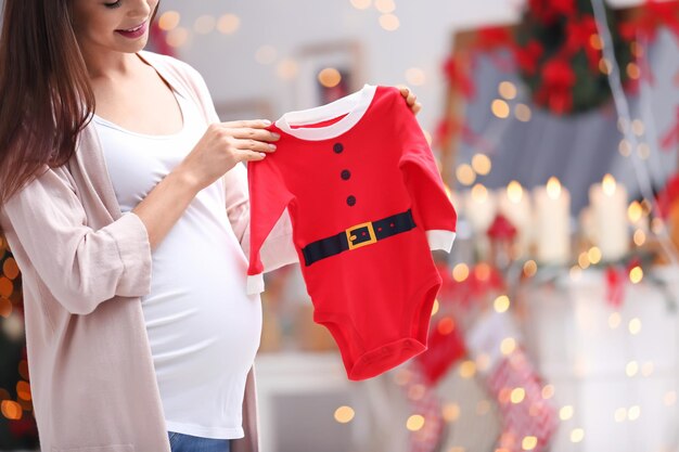 Heureuse femme enceinte avec costume de bébé Père Noël dans la chambre décorée pour Noël