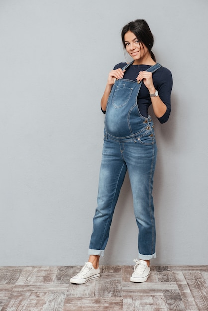 Heureuse femme enceinte debout sur un mur gris.