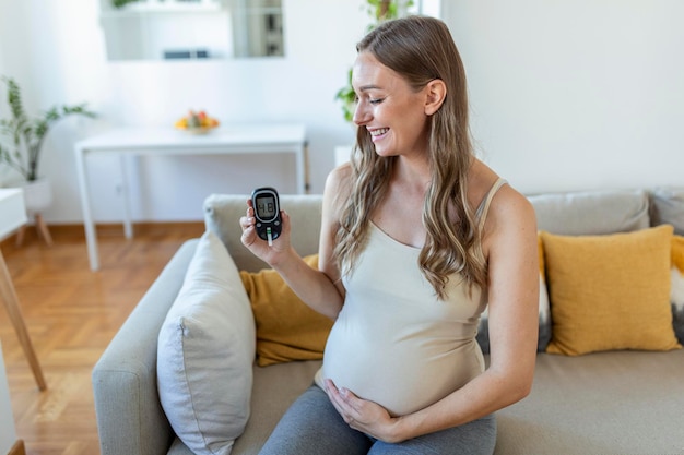 Heureuse femme enceinte avec glucomètre vérifiant la glycémie à la maison. Femme testant une glycémie élevée. Femme enceinte tenant un appareil pour mesurer la glycémie