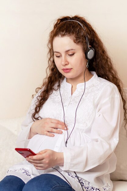 Heureuse femme enceinte avec gros ventre écoutant une musique classique avec des écouteurs au téléphone