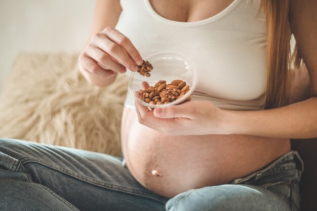 Heureuse femme enceinte à la maison, manger des noix fraîches - amandes, noix. Concept de grossesse en bonne santé.