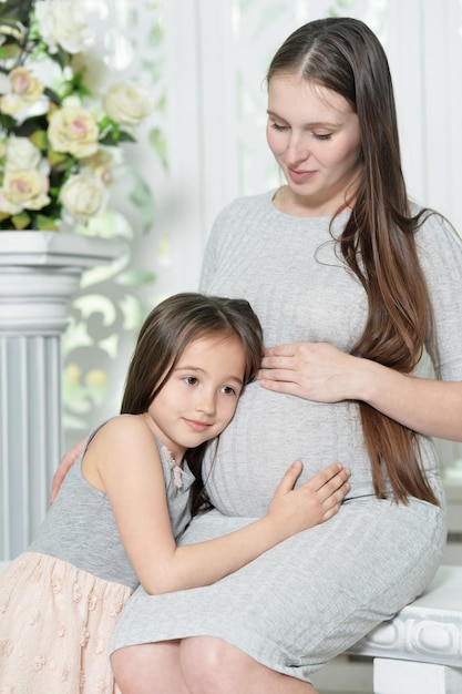 Heureuse femme enceinte avec sa fille posant à la maison
