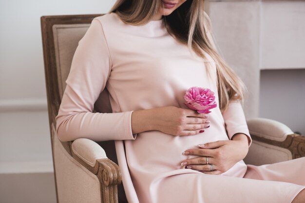 Heureuse femme enceinte tenant le ventre avec une rose rose fraîche