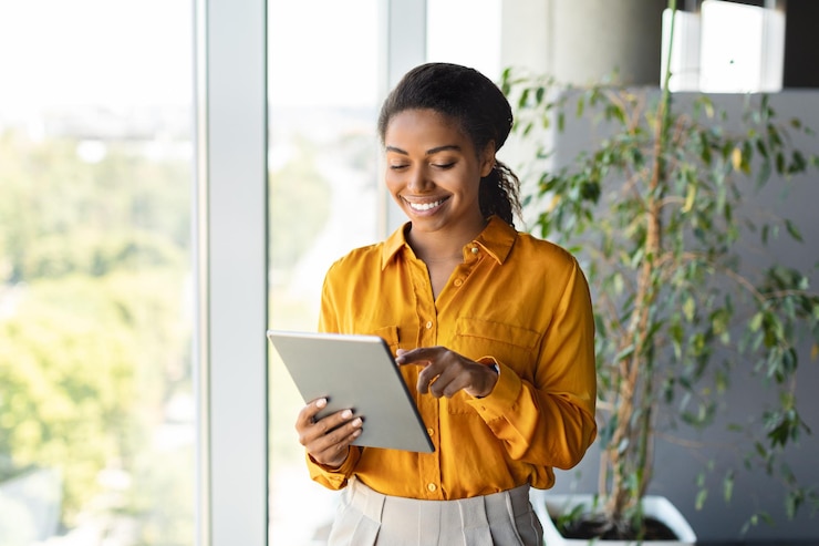 Photo heureuse femme entrepreneure noire utilisant une tablette debout près de la fenêtre dans un espace de copie de bureau de coworking moderne