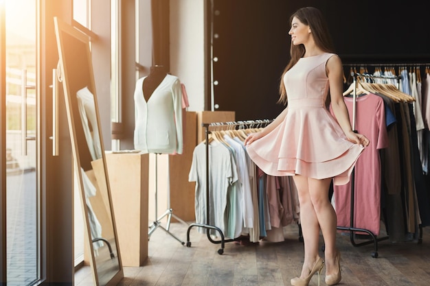 Heureuse femme essayant une nouvelle robe dans la salle d'exposition. Concept de mode et de choix