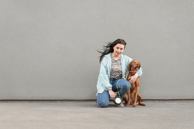 Heureuse femme est assise avec un chien et embrasse un mur gris