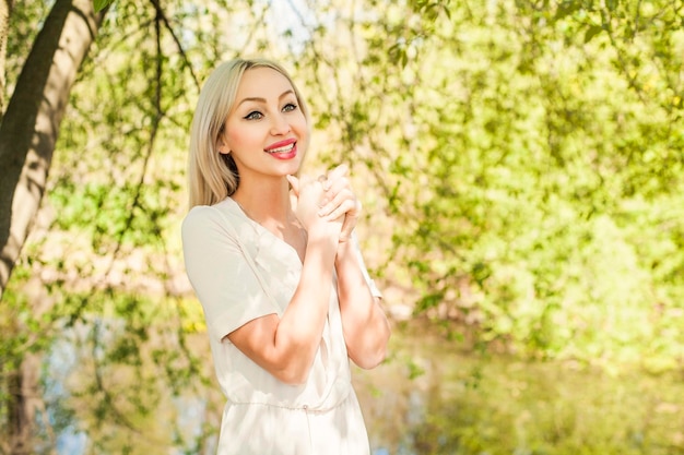 Heureuse femme à l'extérieur sur le feuillage vert laisse fond Modèle féminin cheveux blonds souriant