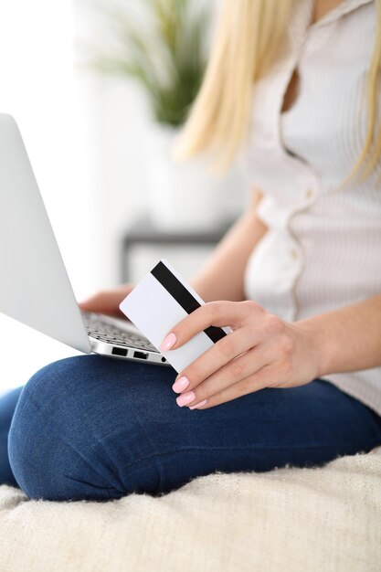 Heureuse femme faisant des achats en ligne à la maison Gros plan d'une main tenant une carte de crédit à côté d'un ordinateur portable