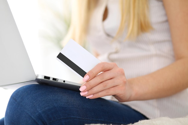 Heureuse femme faisant des achats en ligne à la maison. Gros plan d'une main tenant une carte de crédit à côté d'un ordinateur portable.