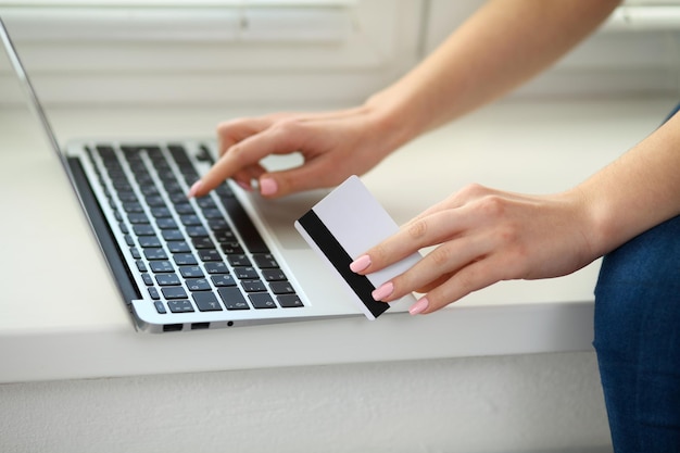 Heureuse femme faisant des achats en ligne à la maison. Gros plan d'une main tenant une carte de crédit à côté d'un ordinateur portable.