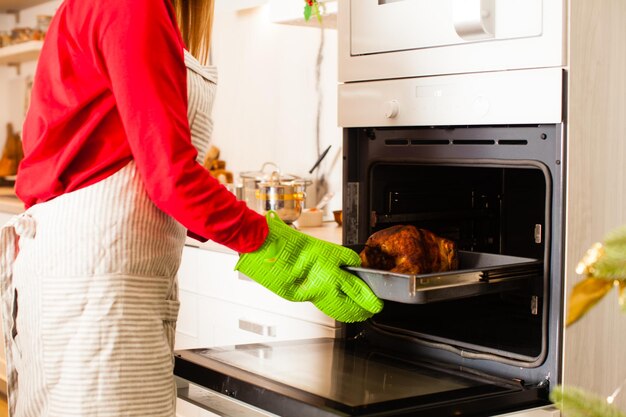 Heureuse femme faisant cuire la dinde de thanksgiving à la cuisine.